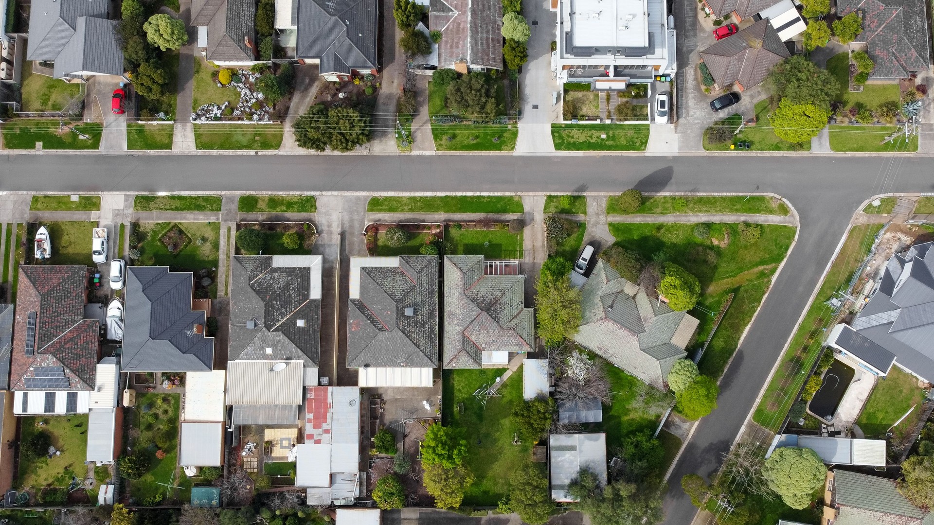 Top down drone view of a small neighborhood of mid-century Australian homes and yards on a quiet street in the outer suburbs of Melbourne